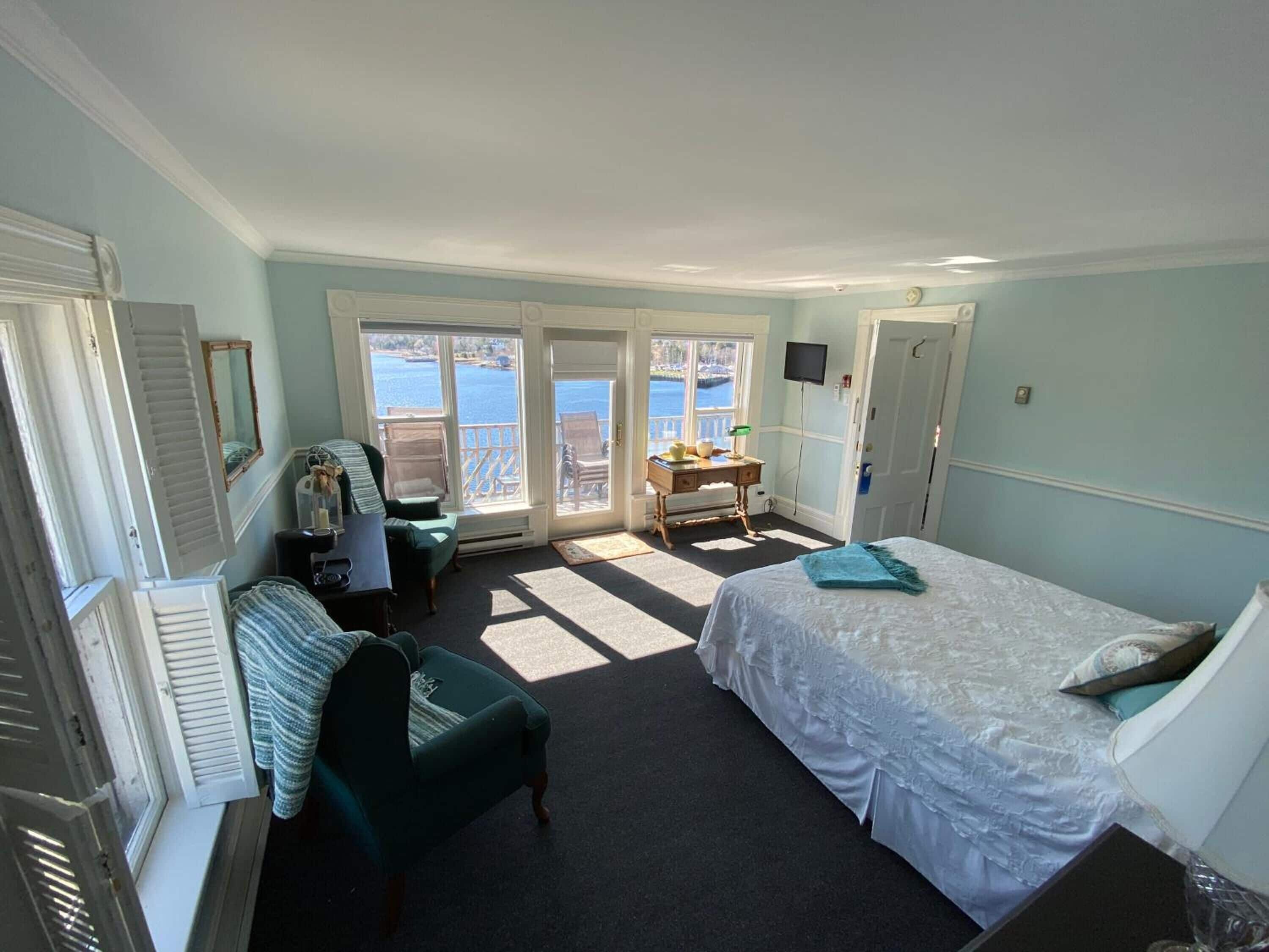 Une chambre à coucher avec un lit, un bureau, une chaise et une vue sur la mer grâce à de grandes fenêtres.