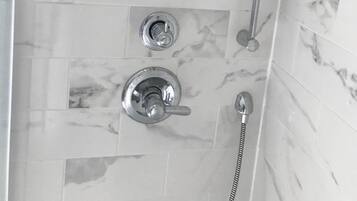 Ein Badezimmer mit Dusche, Duschbrause und zwei Seifenspendern, beschriftet mit „KÖRPER“ und „HAAR“.