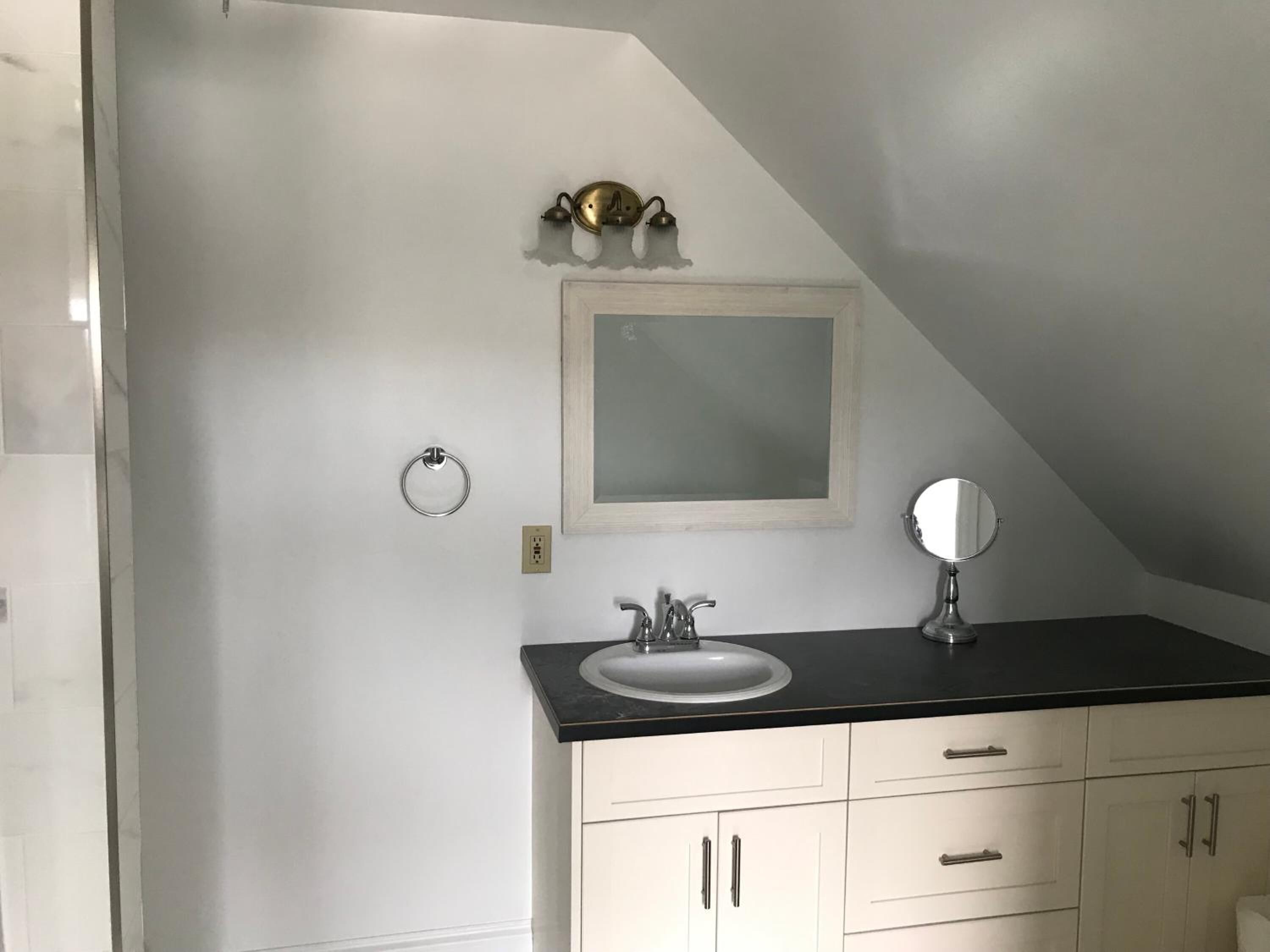 Un baño con tocador blanco, lavabo, espejo y argolla para toallas.