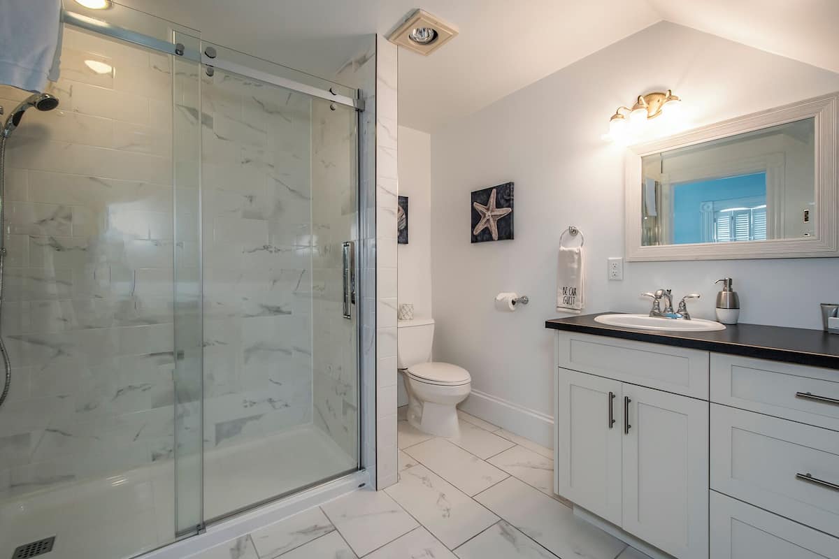 A bathroom with a glass shower enclosure, a toilet, a sink with a mirror, and a towel rack.