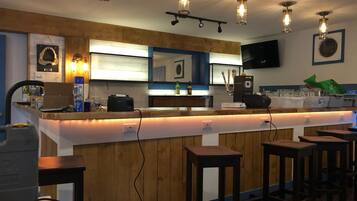 Un espace bar avec des lambris en bois, un comptoir avec des tabourets et un éclairage suspendu.