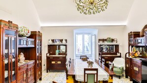 A dining room with a large table, chairs, and a chandelier. There are wooden cabinets and a window with a view.