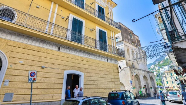A yellow building with balconies, a no parking sign, and a street with cars and pedestrians.