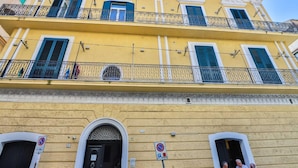 A yellow building with balconies, a black door, and a no parking sign.