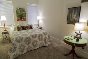 A bedroom with a bed, two bedside tables with lamps, a small round table with a lamp, and framed artwork on the walls. - Waterfront Apartment - Directly on The Ohio River - Downstairs Unit (Jeffersonville)