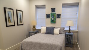 Een slaapkamer met een groot bed, twee nachtkastjes, een raam met jaloezieën en ingekaderde foto's aan de muur.
