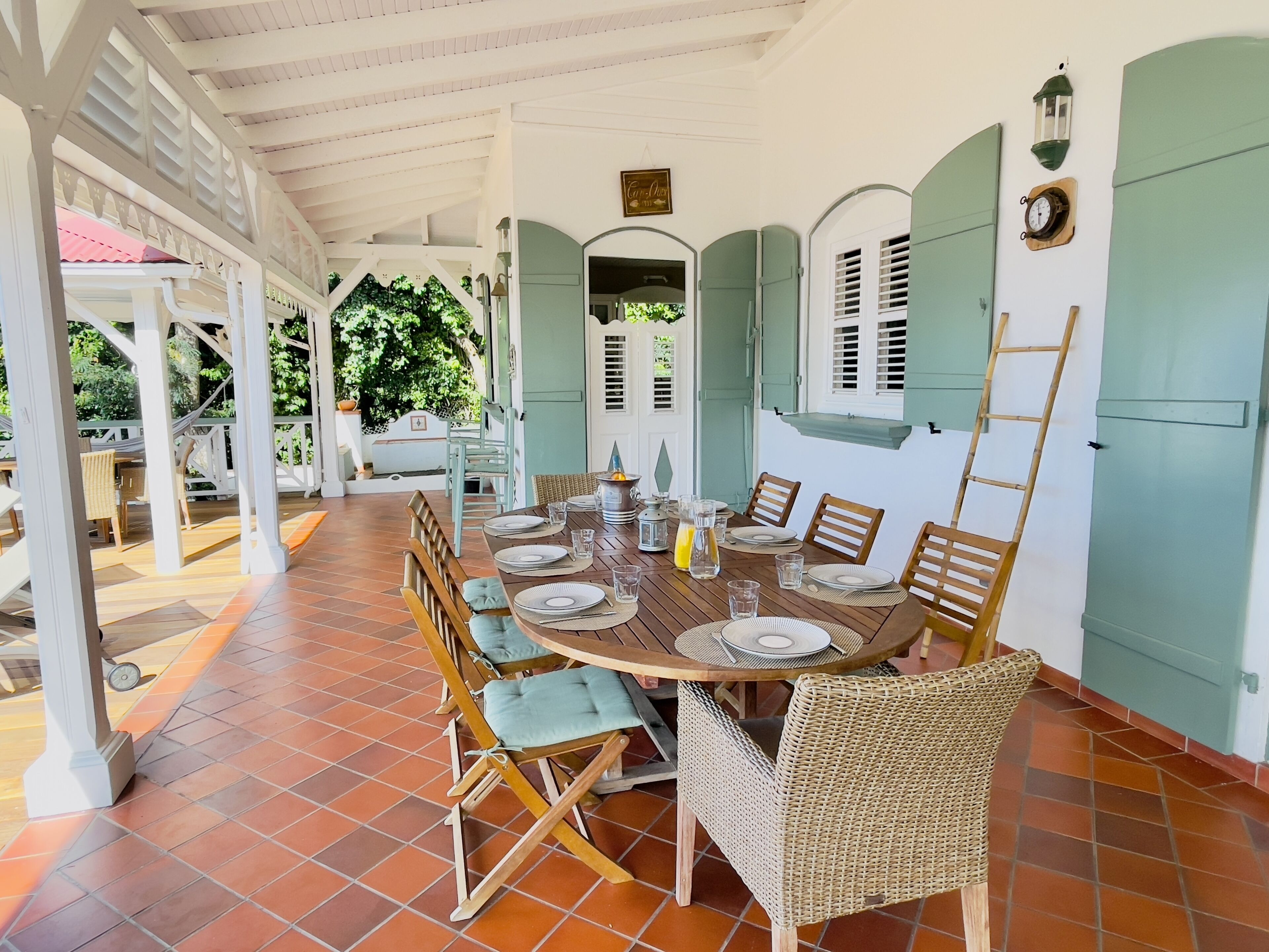 A covered dining area with a long wooden table set for six, surrounded by wicker chairs.