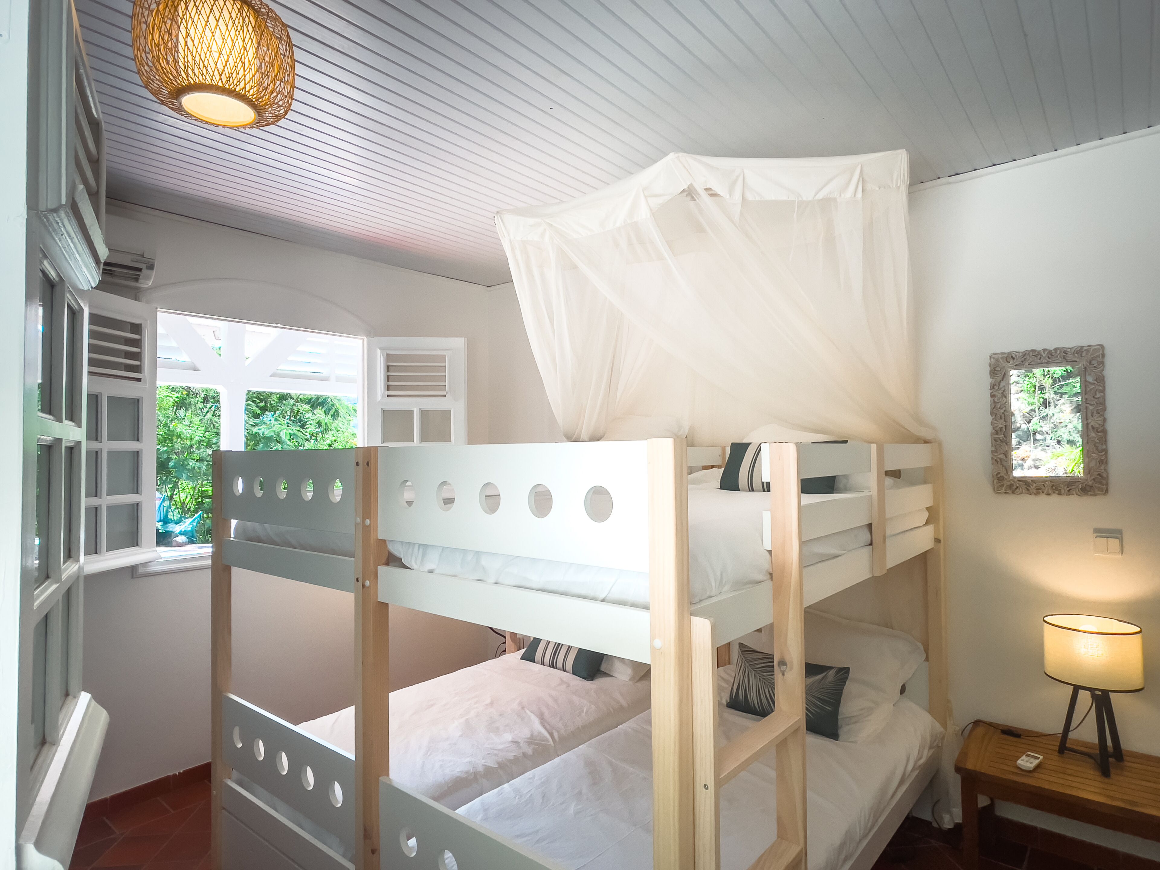 A bunk bed room with a canopy, a window with shutters, a bedside lamp, and a framed picture on the wall.
