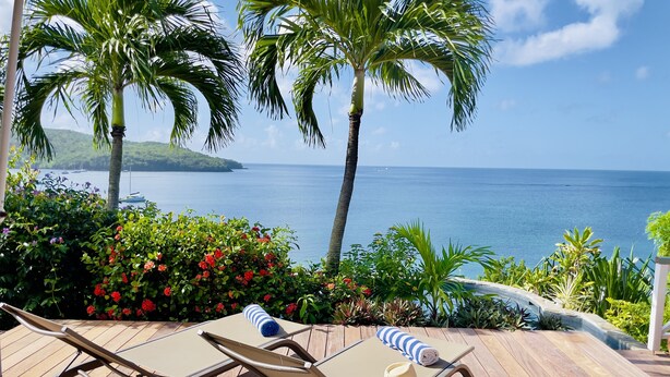 A wooden deck with two lounge chairs and a table, overlooking a clear blue sea and a distant island. - Villa Cap Ouest - Private swimming pool and private sea access - Grande Anse (Les Anses-d'Arlet)