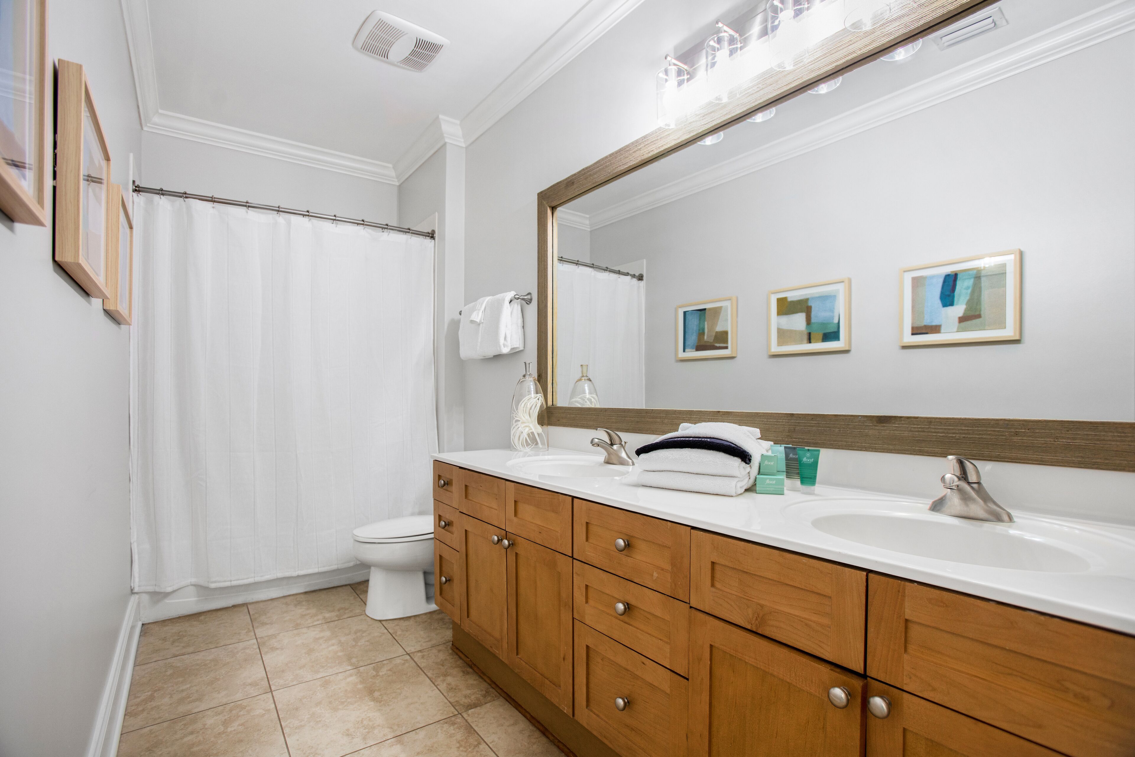 A bathroom with a wooden vanity, two sinks, a large mirror, and a shower curtain.