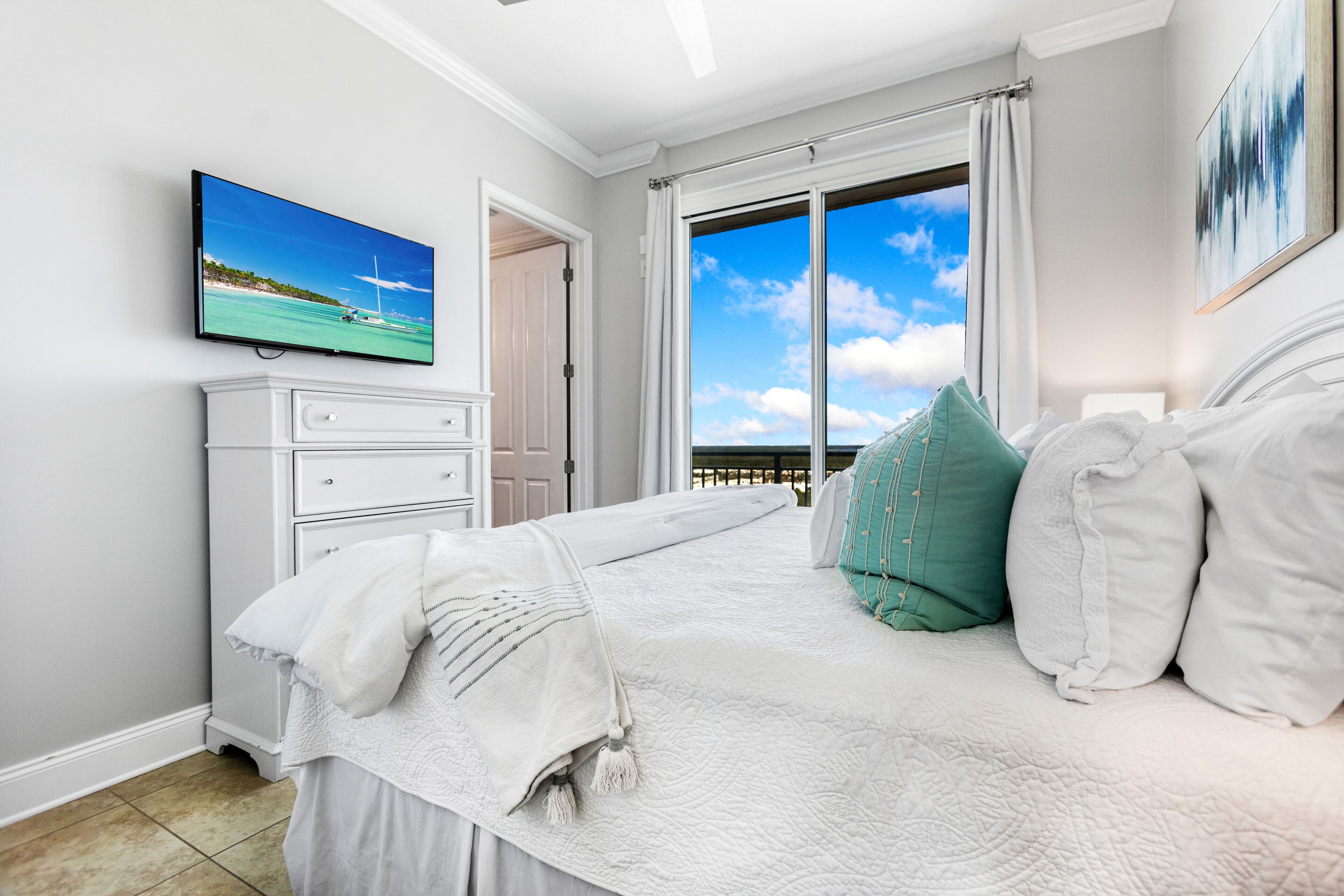 Un dormitorio con una cama grande, un televisor en la pared y vistas al océano a través de la ventana.
