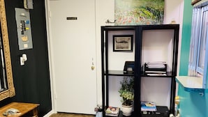 Un pasillo con una puerta blanca que indica “PRIVATE”, una estantería negra con un cuadro enmarcado, una pequeña mesa con objetos y un armario azul.