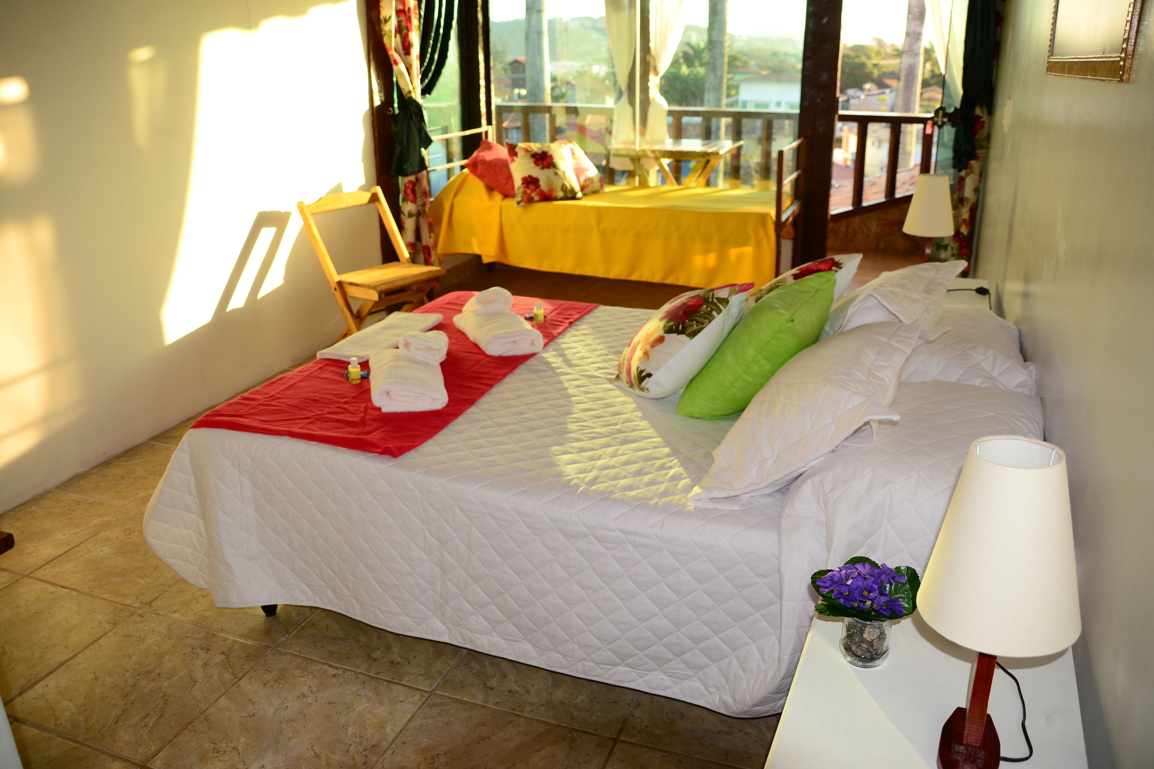 Una camera d'albergo con un letto, un comodino con una lampada, una piccola pianta e vista sull'esterno.