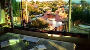 Una habitación con cama, ventana que ofrece vistas a una zona residencial y balcón con barandilla.