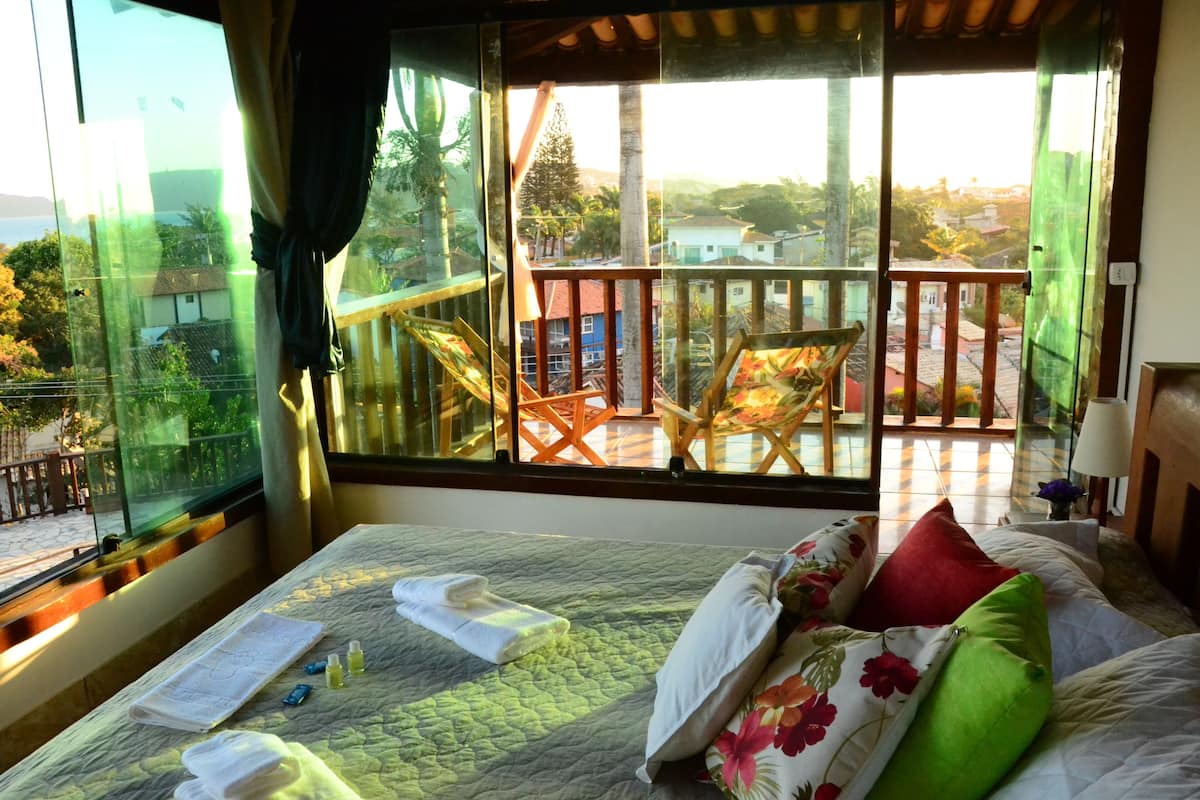 A hotel room with a large window, a bed with floral bedding, and a view of a balcony with outdoor furniture.