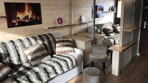 A cozy room with a fur-covered sofa, a small round table, and a mirror reflecting the room. - Studio 5 people south balcony (La Toussuire)