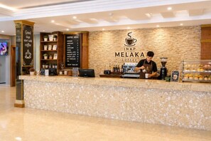 A coffee shop counter with a stone-textured countertop, a coffee menu, and a barista at work. - INAP Melaka - Suites & Living (Malacca City)