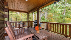 A wooden deck with a table and chairs, a grill, and a view of a forest. - 5BR, 5.5BA log cabin (Nashville)