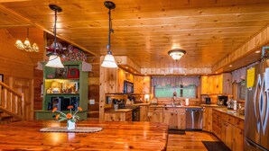 A wooden cabin interior with a central island dining table, kitchen area, and wooden ceiling. - 5BR, 5.5BA log cabin (Nashville)
