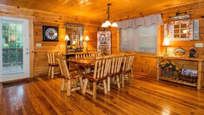 A wooden cabin interior with a dining table and chairs, a clock on the wall, and a welcome sign. - 5BR, 5.5BA log cabin (Nashville)