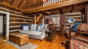 L’intérieur d’une cabane en rondins, avec un escalier en bois, un canapé, des fauteuils à motifs et une malle en bois.