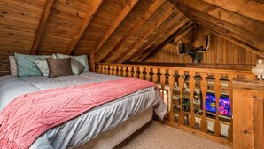 Une chambre avec un plafond en bois, un lit recouvert d’une couverture rose et une tête de cerf fixée au mur.
