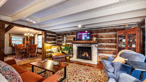 A cozy living room with a fireplace, a television, and comfortable seating. - Walk to Nashville | Hot Tub, Creek Views & Cozy Log Cabin 2BR , 2BA (Nashville)