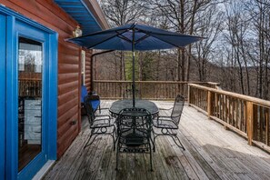 A wooden deck with a table and chairs, a blue umbrella, and a wooden railing.