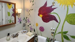 Een badkamer met een grote bloemenmuur, een wastafel met spiegel en een handdoekrek.