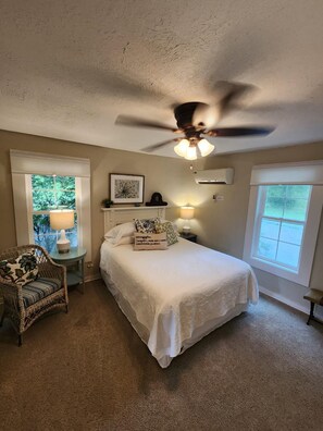 A bedroom with a bed, a ceiling fan, a window, and a chair.