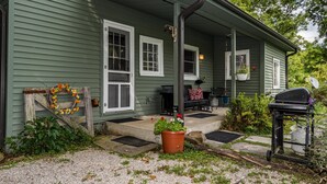 Een groene woning met veranda, houten hekwerk, een bloempot en een barbecue.