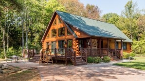 A log cabin with a porch, a picnic table, and a swing set. - Private Log Cabin Retreat | Pond, Hot Tub, Game Room, Sleeps 8 (Columbus)