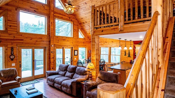 A spacious wooden cabin interior with a large living area, a dining area, and a staircase leading to an upper level. - Private Log Cabin Retreat | Pond, Hot Tub, Game Room, Sleeps 8 (Columbus)