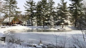 A cabin surrounded by snow-covered trees and a frozen lake. - Private Log Cabin Retreat | Pond, Hot Tub, Game Room, Sleeps 8 (Columbus)