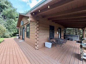 A wooden deck with a covered patio area, outdoor seating, and a barbecue grill.