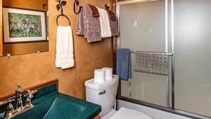 A bathroom with a wooden vanity, a toilet, a shower with a glass door, and a towel rack. - Cozy Pondside Cabin w/ Hot Tub | Near Bloomington & Nashville (Nashville)