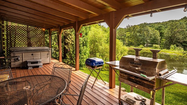 A covered outdoor area with a grill, a barbecue table, and a seating area with a metal chair and a table. - Cozy Pondside Cabin w/ Hot Tub | Near Bloomington & Nashville (Nashville)