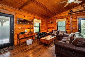 A cozy cabin interior with wooden walls, a fireplace, a sofa, and a dining table. - Cozy Pondside Cabin w/ Hot Tub | Near Bloomington & Nashville (Nashville)