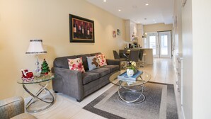 A modern living room with a grey sofa, glass coffee table, and a dining area in the background. - Promo Holidays!2Beds2Bath6PPL Banff Close Gem in Mountain View Townhouse (Harvie Heights)