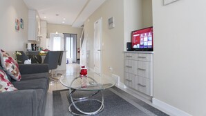 A modern living room with a glass coffee table, a sofa, and a TV on a cabinet. - Promo Holidays!2Beds2Bath6PPL Banff Close Gem in Mountain View Townhouse (Harvie Heights)