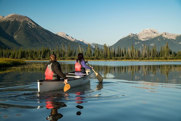 Dos personas en una canoa en un lago tranquilo con montañas al fondo.