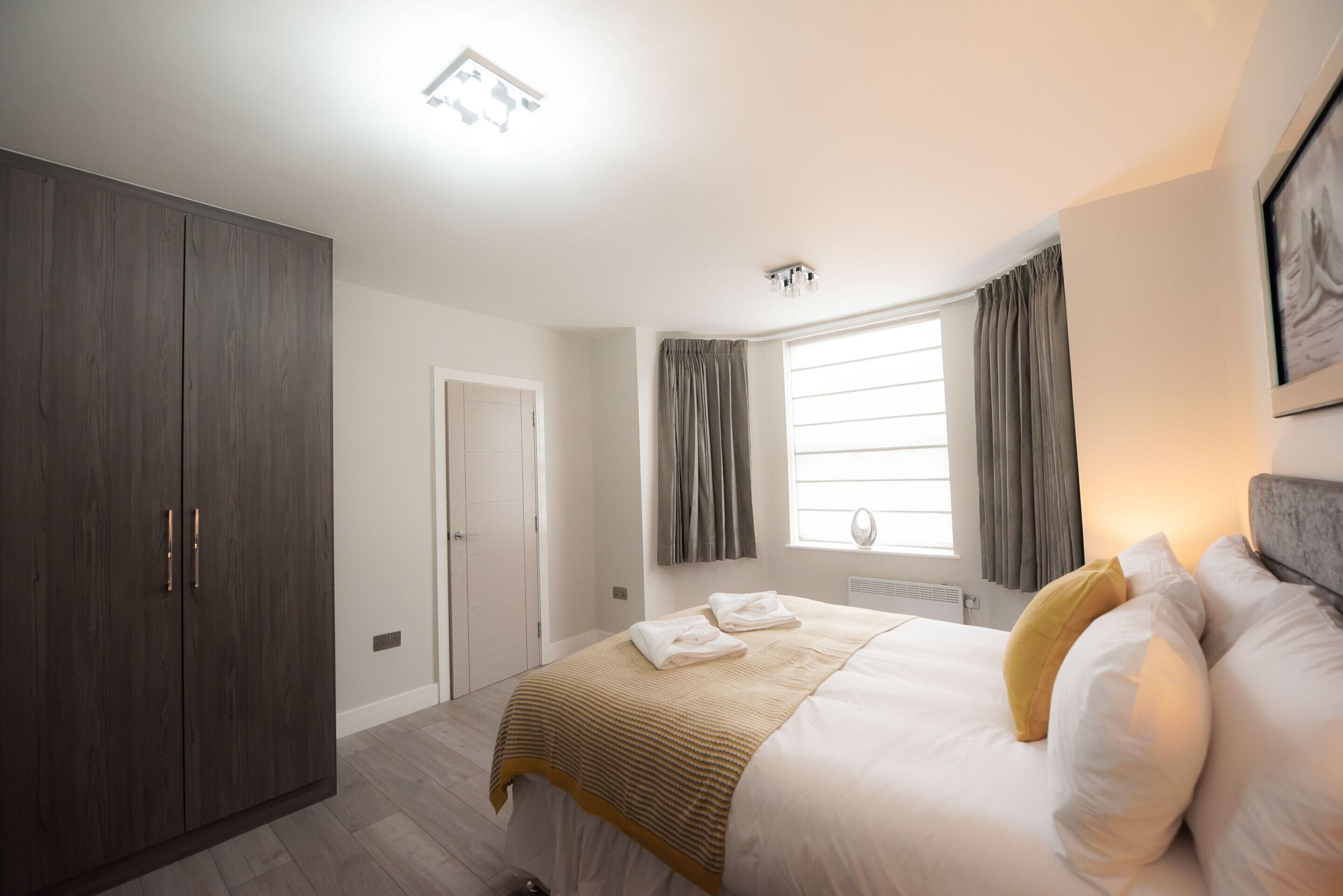 A bedroom with a bed, a wardrobe, a window with curtains, and a ceiling light.