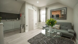 A modern living room with a grey sofa, a glass coffee table, and a kitchen area with grey cabinets and a white countertop. - Laurel House (Reading)