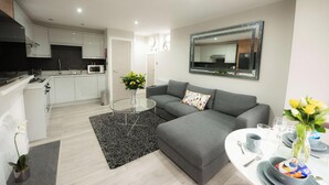 A modern living room with a grey sofa, a glass coffee table, and a dining area with a white table set for two. - Laurel House (Reading)