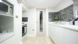 A modern kitchen with white cabinets, a stainless steel oven, and a tiled backsplash. - Laurel House (Reading)