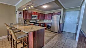 A kitchen with a central island, bar stools, a microwave, oven, washing machine, and a refrigerator. - Oceanfront Dunes B406 + Free Seasonal Beach Loungers (Panama City)