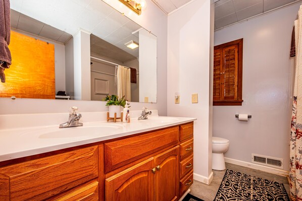 A bathroom with a wooden vanity, two sinks, a mirror, and a toilet.