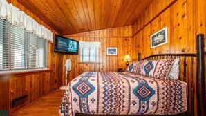 Ein Zimmer mit Holzwandverkleidung, einem Bett, einem Fernseher und einem Fenster mit Jalousien.