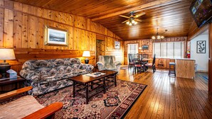 Ein Blockhaus-Interieur mit Holzbalkendecke, einer großen Couch, einem Essbereich und einer Küche.