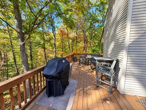 A wooden deck with a barbecue grill, outdoor furniture, and a view of a forested area.